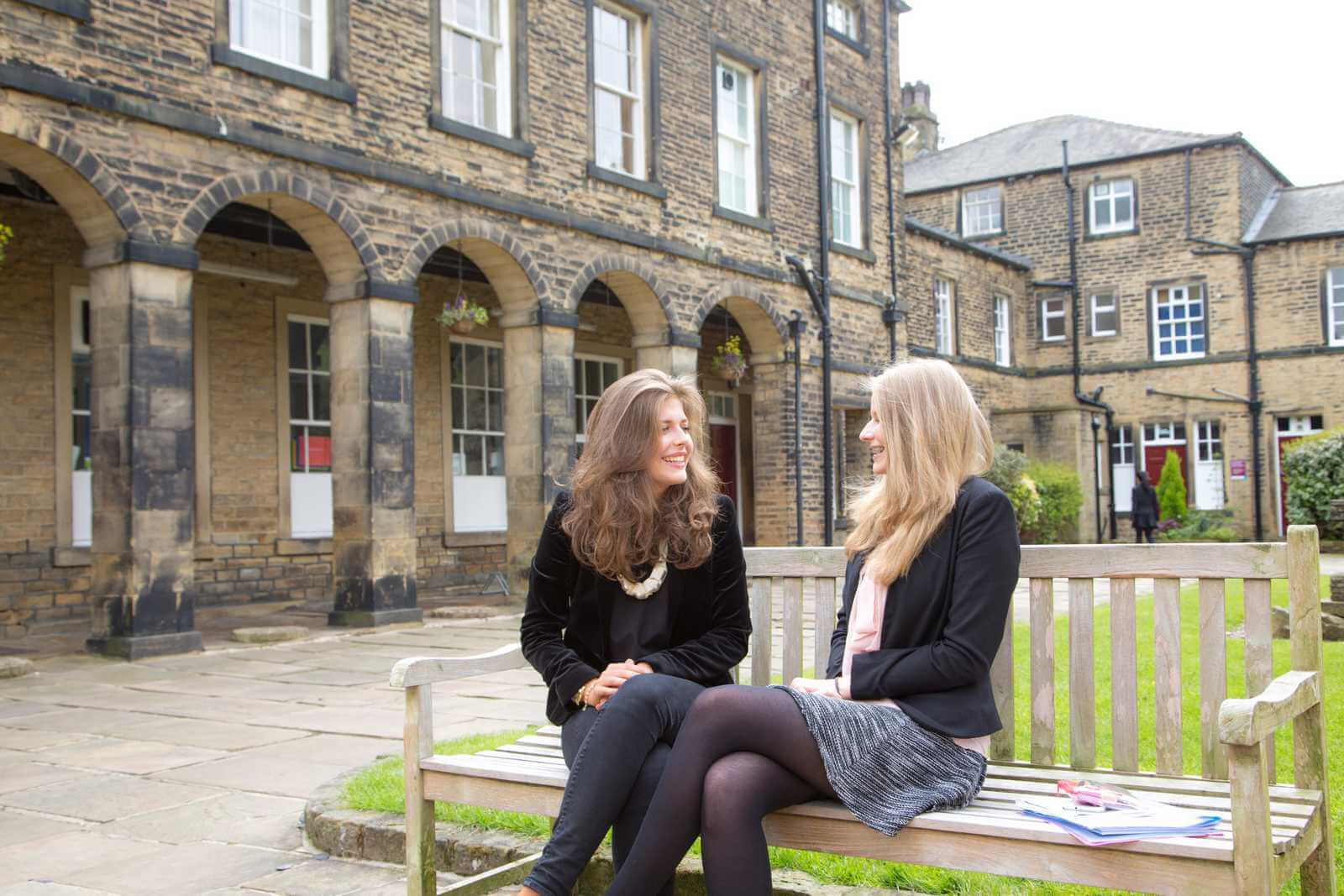 Aufenthalt im privaten Internat – zwei Schülerinnen auf einer Bank im Innenhof einer britischen Boarding School